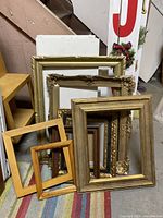 Multiple vintage picture frames stacked and leaning showing variety of sizes and styles.