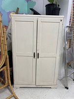 Closed view of the vintage white wooden wardrobe cabinet with two paneled doors and metal handles.