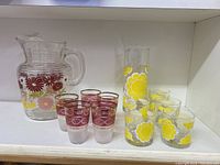 Wide shot showing the entire vintage glassware collection on a shelf, including the pitcher, six red floral tumblers, one tall yellow floral glass, and four small yellow floral tumblers.