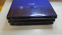 Three closed blue Asus laptops stacked on top of each other.