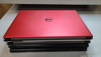 Four Dell Inspiron 15 laptops stacked showing one red laptop lid on top