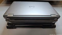 Four Dell Vostro laptops stacked closed showing silver top plating and some wear.