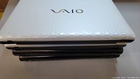 Stack of 4 Sony VAIO laptops closed showing white top laptop with VAIO logo.