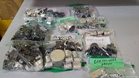 Wide overview of multiple plastic bags filled with various audio component parts including knobs and dials, showing quantity and variety.