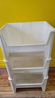 Stacked white plastic storage bins against yellow wall on wooden floor showing three bins stacked securely.