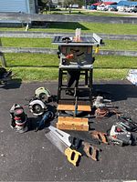 Overview of all tools laid out including table saw on stand, saws, sanders, hand saws and miter boxes