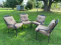Four metal lawn chairs arranged on grass with cushions attached, showing overall set.