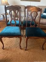 Four wood dining room chairs with green velvet-like upholstery and carved backs arranged in living room.