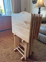 Side view of the wooden folding tables stacked upright on the storage rack, showing wood grain and foldable legs.