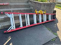 Full view of the 8 ft fiberglass step ladder lying horizontally on the ground near steps, showing red side rails and white rungs.