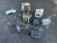 Overview of lot items arranged on ground including Stanley booster pack in box, battery charger boxes, towing mirrors, tire inflator, and tire totes.