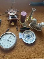 Full lot overview showing wooden cuckoo clock with pendulum and pinecone weights, silver quartz clock, decorative plate clock, eagle bookends, candle holders, and desk clock with pens.