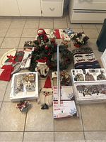 Overview photo showing all items arranged on tile floor including storage totes, village decorations, wreaths, linens, Santa figurines, lights, utensil holder and more.