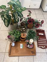 Full lot arranged on tiled floor including largest artificial plant on left, wicker basket arrangement in center with birdhouse, wooden calendar on right, wooden tray in front with candle and vase, medium wooden container, smaller plants and greenery clusters.