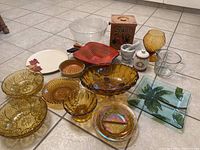 Full lot overview showing large clear glass salad bowl, amber glass serving dishes, wooden basket, pottery items, mortar and pestle, cookie jar, measuring cup and garlic keeper.