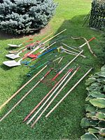 Full view of all garden tools laid out on grass including shovels, rakes, hoes, axes, pickaxe, scythe, and magnetic broom.