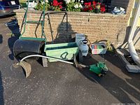 Full lot overview showing lawn roller, green lawn spreader, garden sprayer, gas weed eater trimmer, and trimmer line tote