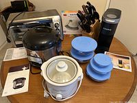 Full lot overview showing Hamilton Beach toaster oven, Wolfgang Puck rice cooker, Taste of Home crock pot, glass food containers, Keurig coffee maker, knife block, kitchen scale in package.