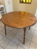 Full view of round solid wood kitchen table with legs attached, seated on tiled floor in a kitchen setting.
