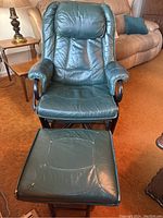 Front view of dark green leather swivel recliner/glider chair and matching ottoman showing minor cracking on leather and wear spots.