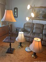 4 lamps shown: 2 table lamps with beige shades, 1 wood floor lamp with built-in table base, 1 silver/chrome 3-light floor lamp