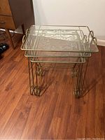 Three vintage nesting side tables stacked together showing gold-tone metal frames and etched glass tops.