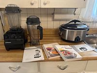 Vitamix base with two blending containers and lids, cookbooks and manuals, Hamilton Beach slow cooker with user manual