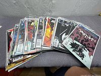 Panoramic view of 12 Batman comic books laid out on fabric surface, all in clear protective sleeves