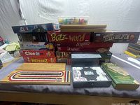 View of stacked board game boxes showing titles Clue, Buzz Word, Scrabble, Yahtzee Texas Hold'em, 4 Letter Words, Hedbanz, Clue Jr., and a large Puzzle box