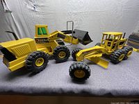 Pair of two vintage yellow metal Tonka trucks side by side on a gray surface