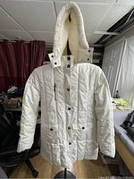 Full front view of white quilted winter coat with button and zip closures, hood, and pockets.