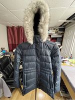Front view of black Tommy Hilfiger winter coat with hood trimmed in light gray faux fur on a hanger