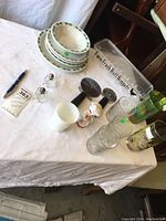 Overview of all items in the lot laid out on a white cloth, showing plates, glasses, egg keeper, salt and pepper shakers, and pizza wheels.