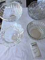 Five clear glass bowls arranged on a fabric surface showing various designs and patterns including scalloped edges and ribbed sides.