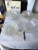 Four clear crystal bowls displayed on a white cloth, showing details of cut and etched patterns with accompanying MaxSold lot tag and a pen for scale.