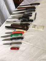 Overview photo of the various knives and kitchen tools laid out on a white surface showing a range of blades and handle colors, including a bread slicer and a multi-tool knife.