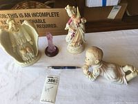 Wide photo showing all four figurines on table with pen for scale.