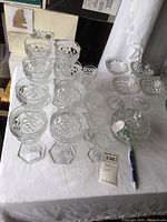 Overview of entire glassware set including water glasses, smaller stemmed glasses, sherbet glasses and lidded candy dish on white cloth.