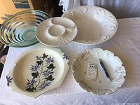 Photo showing five large bowls on a white surface including transparent green glass bowl, textured off-white ceramic bowl, and various floral-themed ceramic bowls