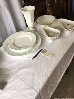 Two similar photos showing all dishes including grape pattern platters, plates, Westmoreland vase, gilt edge bowl, and Hazel-Atlas pear dishes stacked.