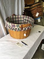 Photo of the large wooden woven basket showing the plaid fabric liner with ruffled edges inside and leather handles on the sides.