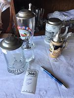 Four lidded German beer steins displayed on white cloth with pen and lot tag
