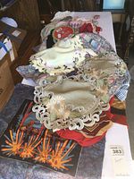 Photo showing various embroidered and cutwork doilies and batik textiles layered on a table along with other mixed fabric items.