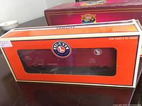 Photo showing Lionel stock car in original box with orange exterior, Lionel logo, and detailed model car visible through window.