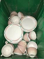 Set of luncheon plates, cups, and saucers piled in a green crate showing color and design details