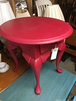 Front angle view of a magenta chalk painted end table with Queen Anne legs and round top.