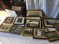 Photo of a variety of old picture frames arranged on a table, showing different sizes and styles with different artwork and photos inside.