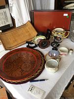 Overview photo showing lacquer trays, wooden bamboo tray, round wooden platter, burgundy cloth, teapot, teacup, creamer, small vase, black decorative item, and small containers with pen and auction tag for scale.