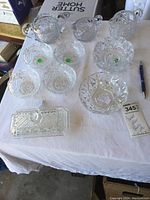Full set of small glass bowls, two creamers, ashtray, and butter dish on a white cloth.
