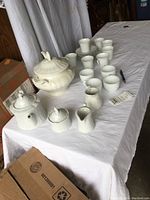 Overview of all items in the lot including Tirschenreuth cups and saucers, soup tureen, ladle, punch mugs, Feltman Bavaria teapot, sugar bowl, and creamers on a white sheet-covered table.